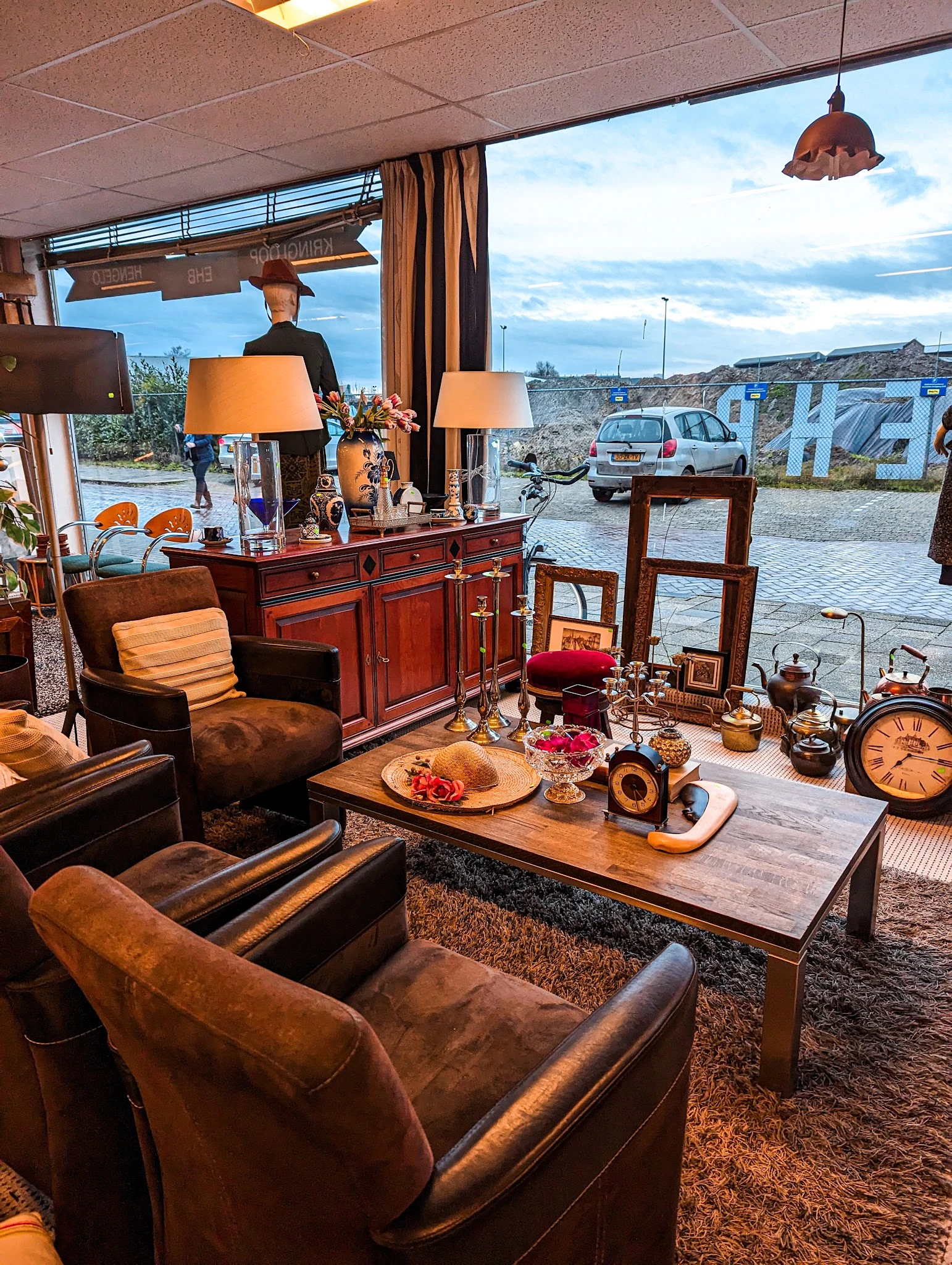 Ingerichte woonkamer met bruinleren fauteuils, houten bureau, tafellamp en decoratiestukken in een kringloopwinkel