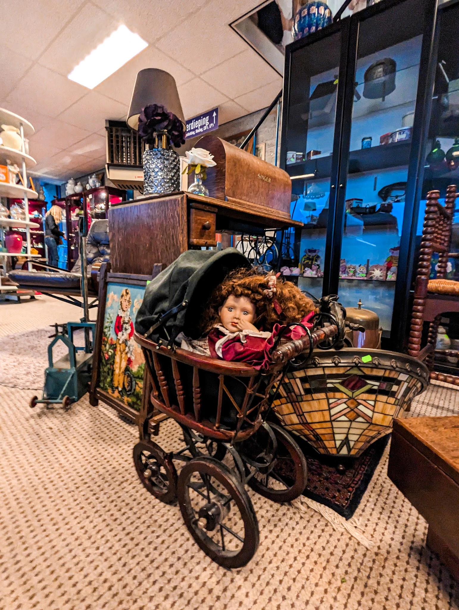 Winkelbinnenkant met vintage kinderwagen en speelgoed tussen meubels en stellingen