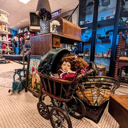Winkelbinnenkant met vintage kinderwagen en speelgoed tussen meubels en stellingen