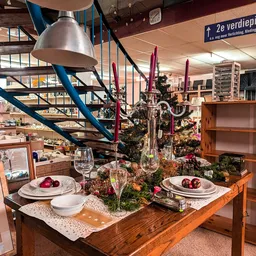 Gedekte tafel met servies, glazen en kaarsen tussen groene planten en decoraties