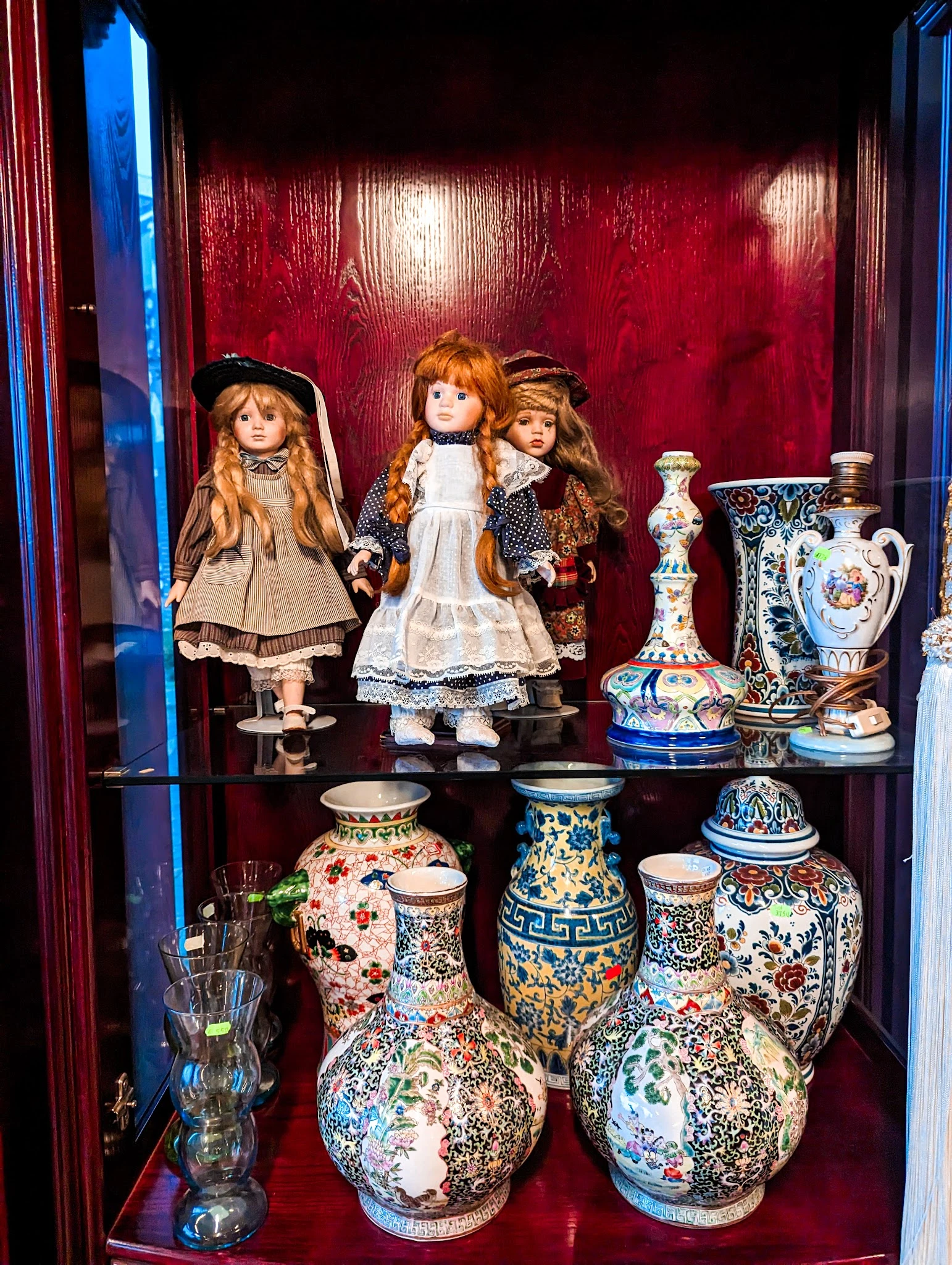 Vitrinekasten met antieke porseleinpoppen, vazen en decoratief porselein op rode achtergrond