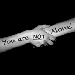 Zwart-witfoto van twee handen die elkaar vasthouden met tekst 'you are NOT alone!' geschreven op de armen