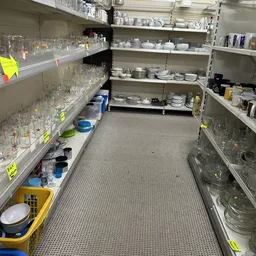 Stellingen met glazen, servies, kopjes en huishoudartikelen in een kringloopwinkel