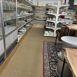 Winkelinterieur met stellingen vol porseleinen servies en huishoudartikelenAan beide zijden zijn witte stellingen zichtbaar m