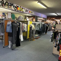 Winkelvloer met rekken vol tweedehands kleding, gele displaystandaard in het midden, verlichting van boven