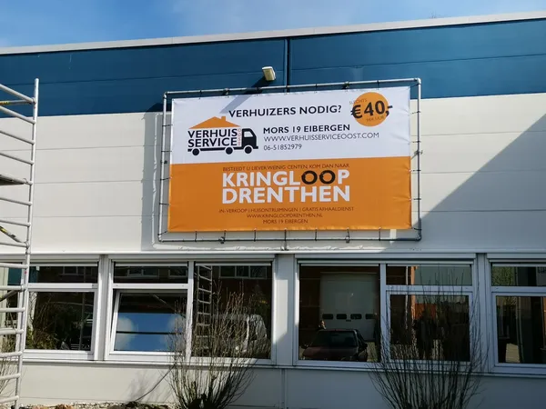 Gevel van kringloopwinkel met wit-blauwe pui en groot oranje reclamebord voor verhuisservice