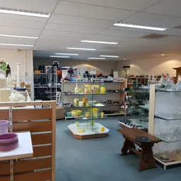 Winkelvloer met glazen vitrines, houten tafels en stellingen vol serviesgoed en huishoudartikelen