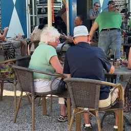 Bezoekers zitten aan tafels op een terras bij de winkel
