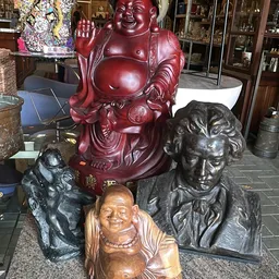 Verzameling beelden en sculpturen: rode Boeddha-buste, houten en bronzen portretten.