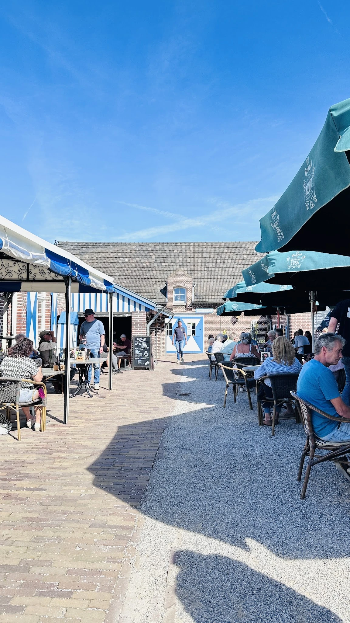 Terras met blauwe parasols waar bezoekers zitten te eten en drinken in de zon