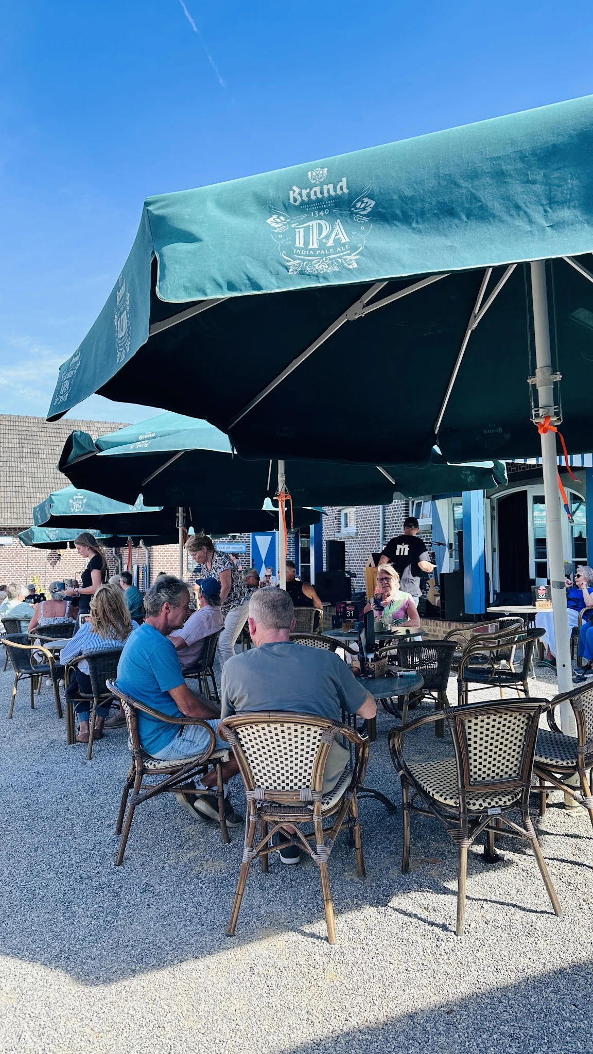 Terras met zwarte parasols waar bezoekers zitten aan tafels met stoelen, blauwe gebouwen op de achtergrond