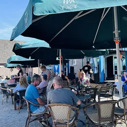 Terras met zwarte parasols waar bezoekers zitten aan tafels met stoelen, blauwe gebouwen op de achtergrond