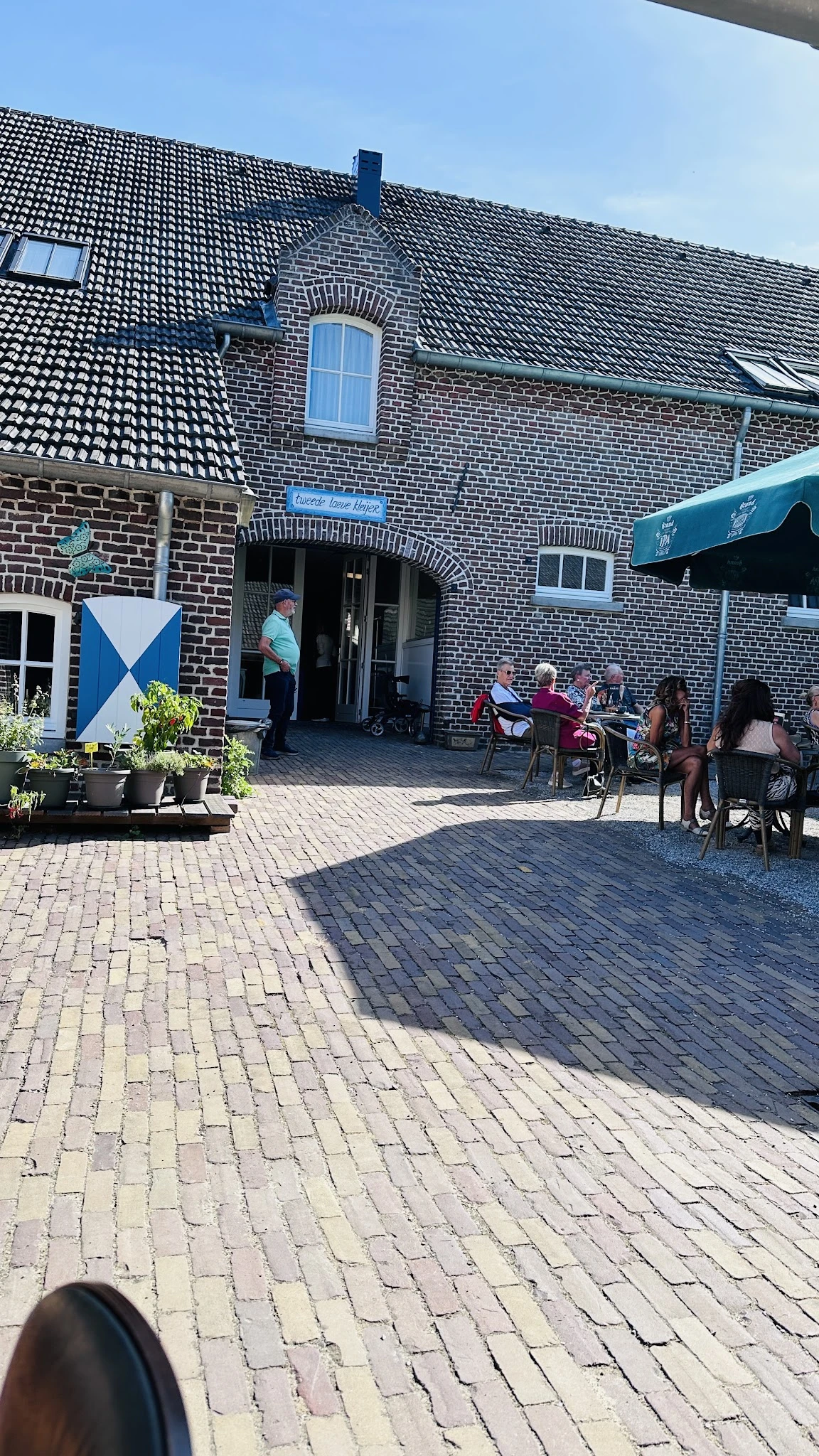 Terras buiten met bezoekers aan tafels onder parasol bij bakstenen gebouw