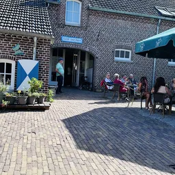 Terras buiten met bezoekers aan tafels onder parasol bij bakstenen gebouw