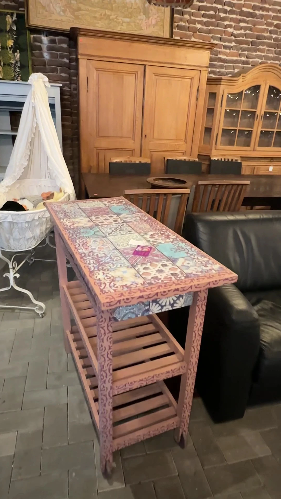 Roze beschilderde houten tafel met kleurig tegelwerk op het blad, in een interieur met houten stoelen op de achtergrond