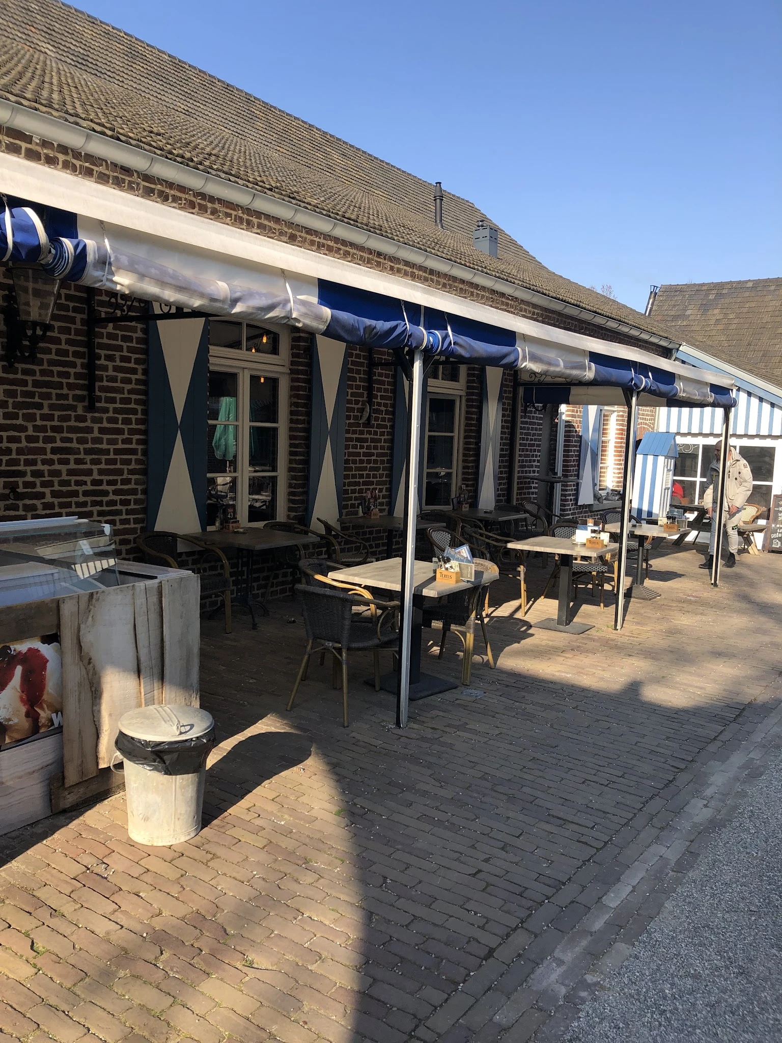 Terras met tafels, stoelen en blauwe parasols buiten een bakstenen gebouw