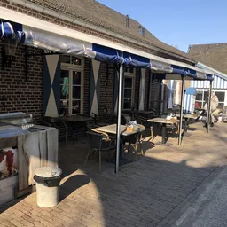 Terras met tafels, stoelen en blauwe parasols buiten een bakstenen gebouw