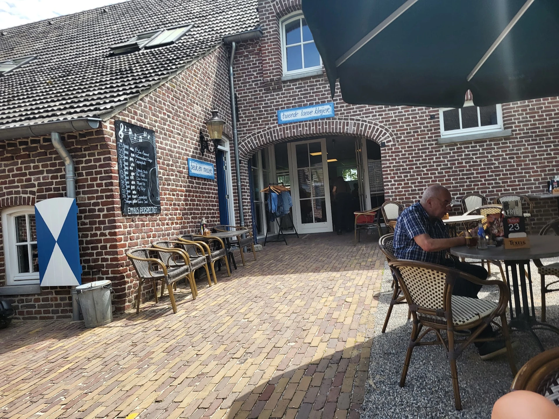 Terras buiten een bakstenen gebouw met tafels, stoelen en een man aan het werk achter de balie