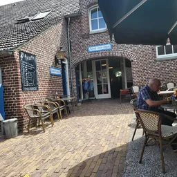 Terras buiten een bakstenen gebouw met tafels, stoelen en een man aan het werk achter de balie