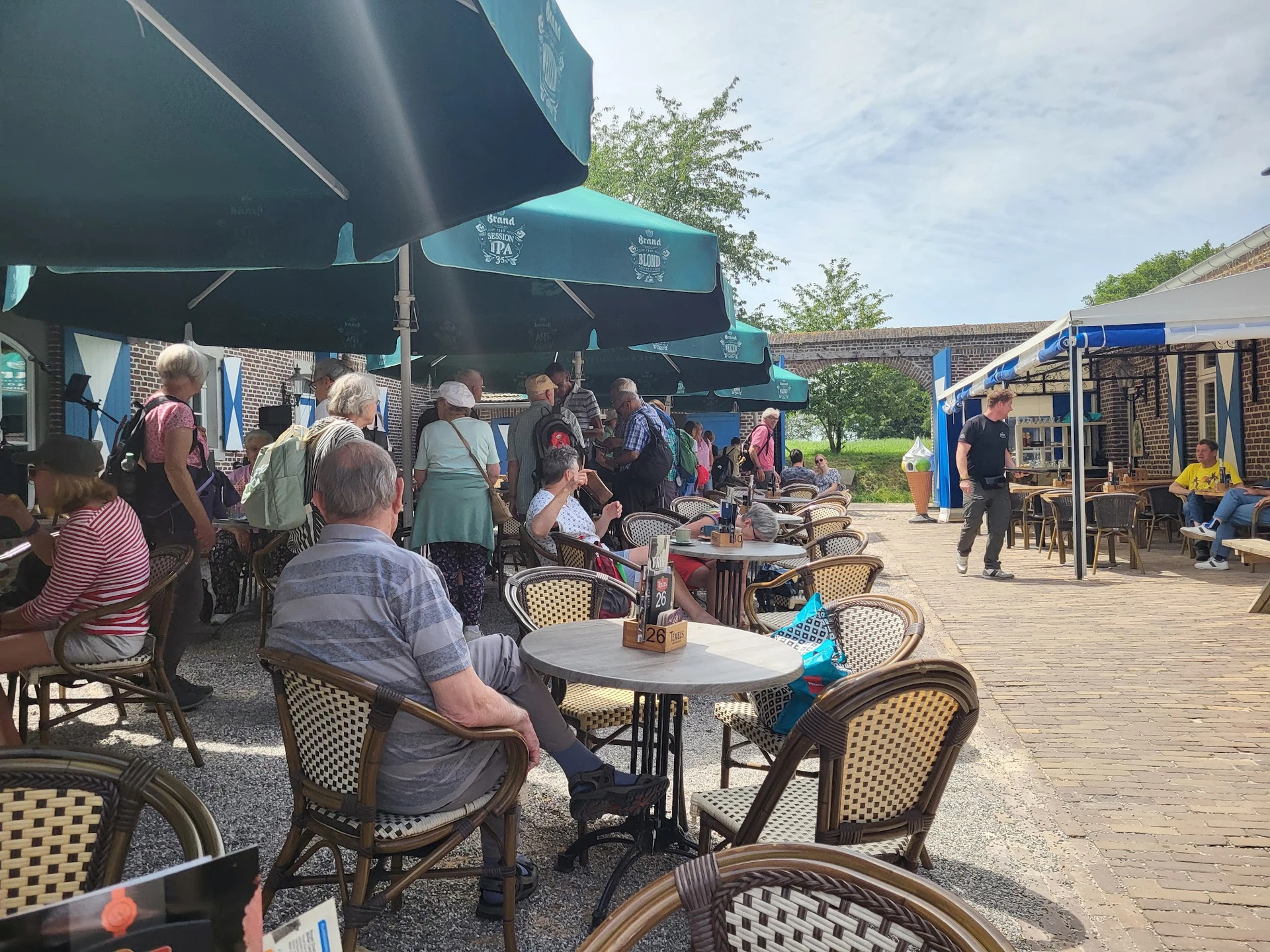 Terras met bezoekers onder blauwe parasol, tafels en stoelen op houten platform