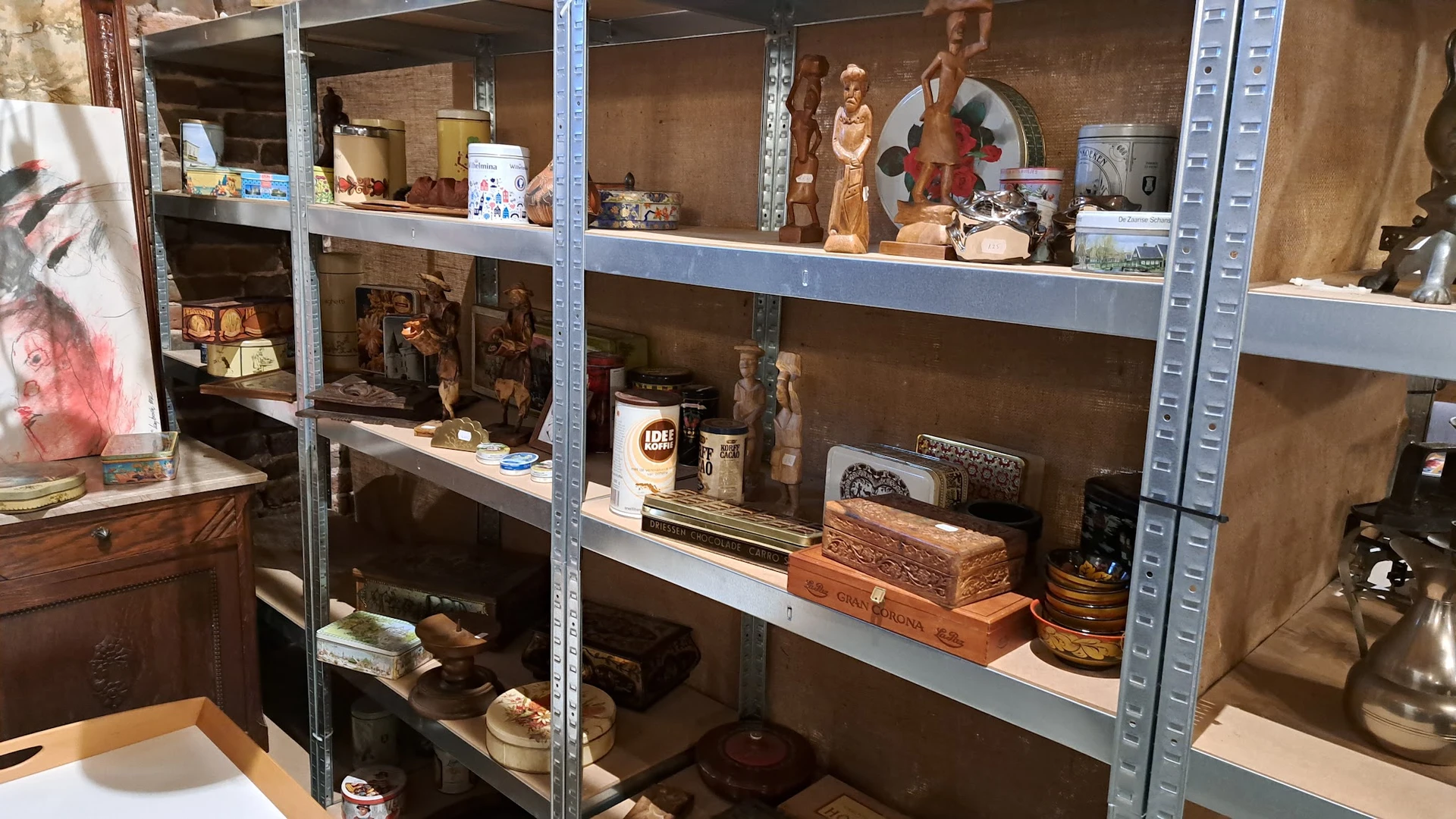 Stellingen met decoratieve items zoals houten beelden, servies, dozen en diverse huishoudartikelen