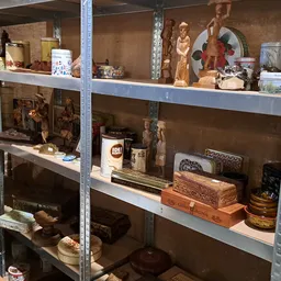 Stellingen met decoratieve items zoals houten beelden, servies, dozen en diverse huishoudartikelen