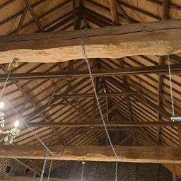 Houten dakconstructie met balken en hangende kettingen in een schuur of boerderijgebouw