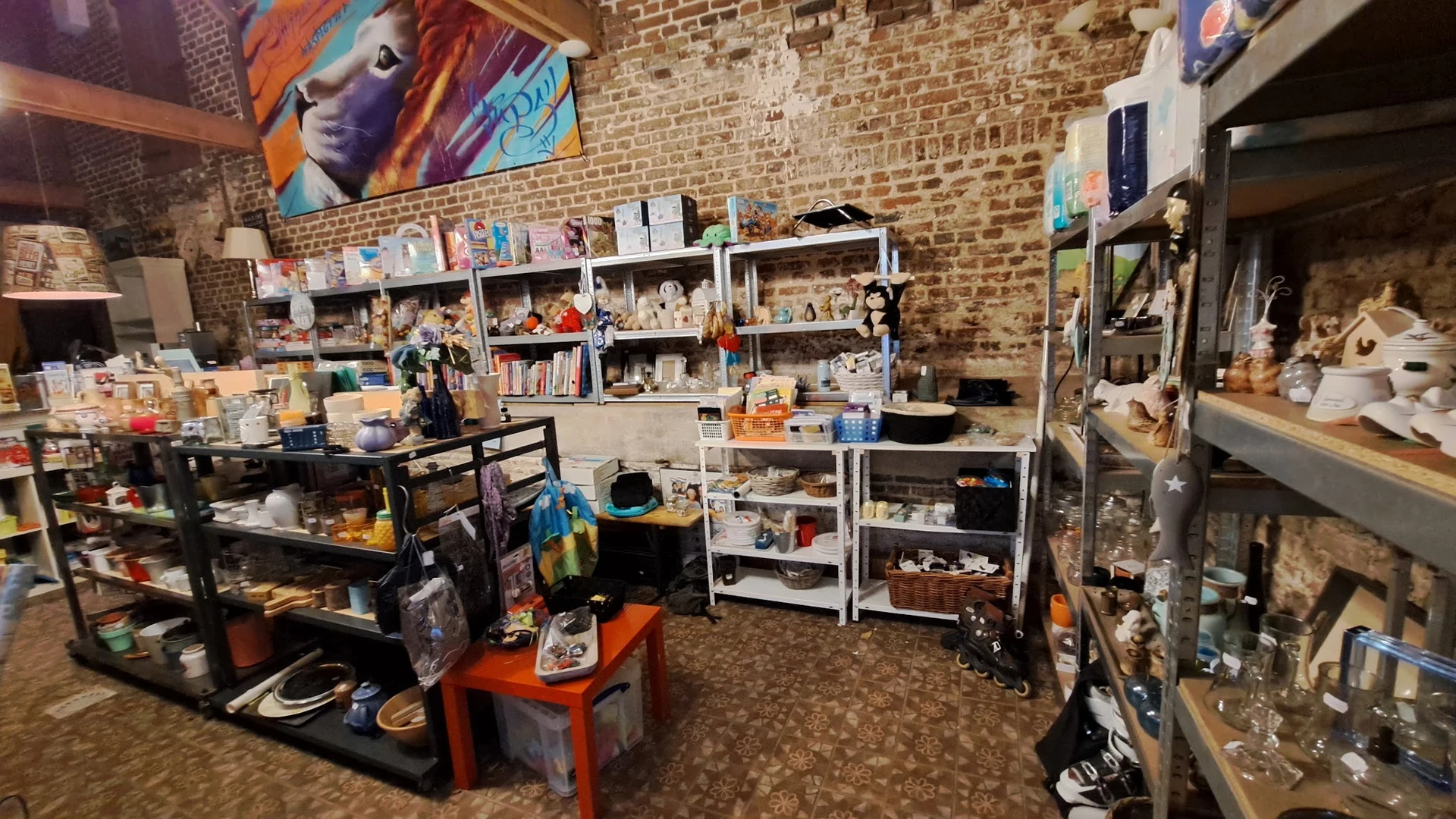Winkelinterieur met stellingen vol spullen, tafels met voorwerpen, bakstenen muur en kleurrijke kunst aan de muur