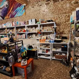 Winkelinterieur met stellingen vol spullen, tafels met voorwerpen, bakstenen muur en kleurrijke kunst aan de muur
