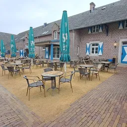 Terras met tafels, stoelen en blauwe parasols tegen een bakstenen gebouw