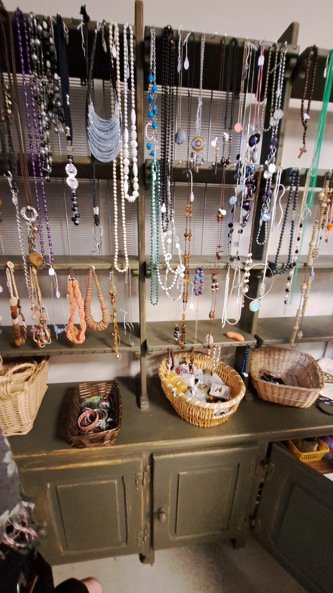 Uitgestalde sieraden en kettingen aan draadrek met wikkelmand vol items eronder