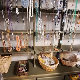Uitgestalde sieraden en kettingen aan draadrek met wikkelmand vol items eronder