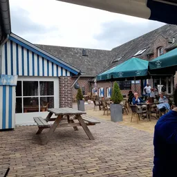 Terras met tafels en stoelen onder groene parasols, bezoekers zitten buiten te eten en drinken