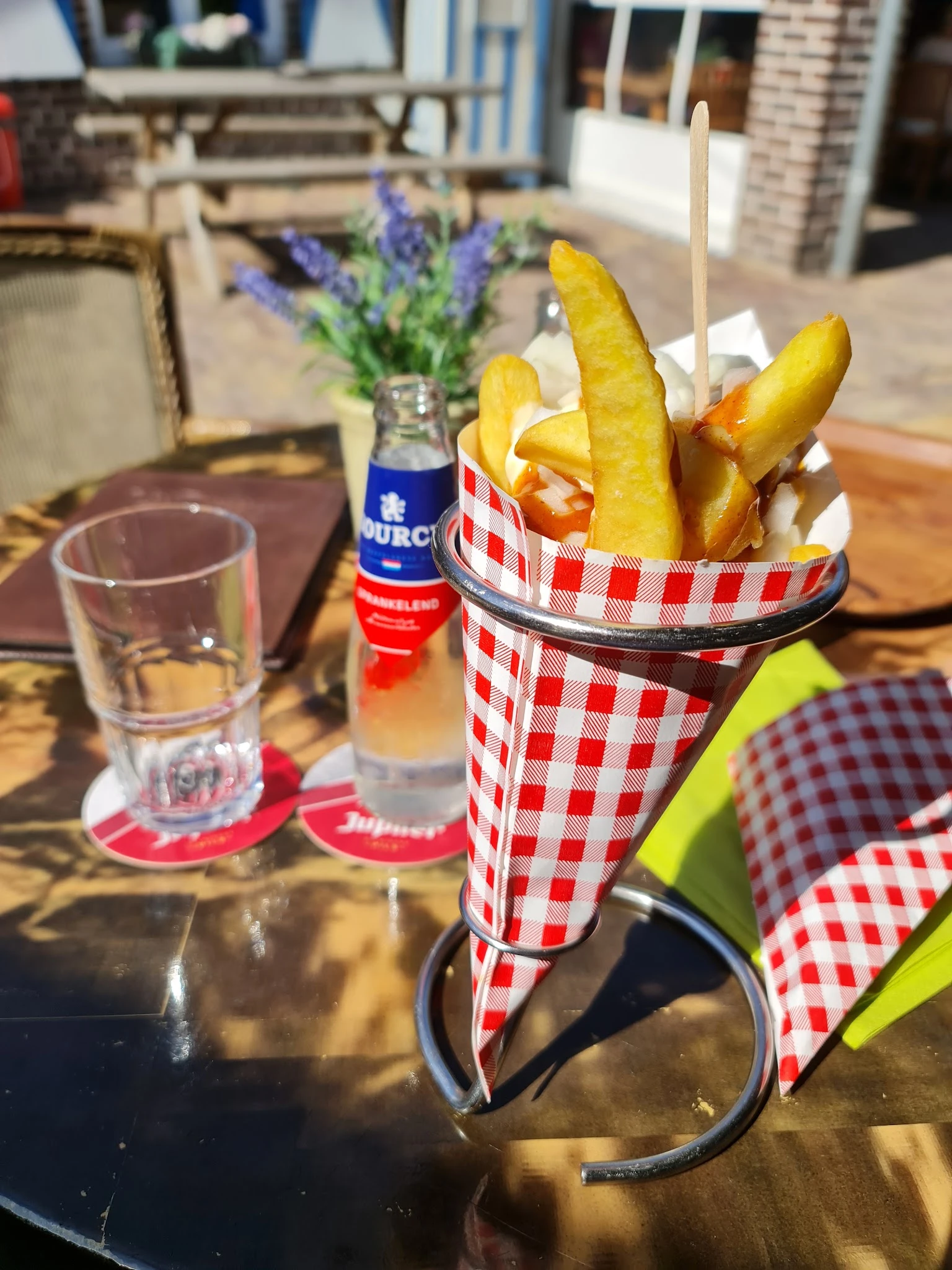 Friet in rood-wit geruite papieren zak met glas water en flesje op tafel