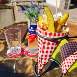 Friet in rood-wit geruite papieren zak met glas water en flesje op tafel