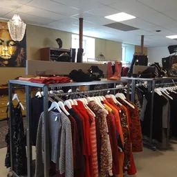 Rekken met tweedehands dameskleding in verschillende kleuren, vooral rode en gekleurde items op hangers uitgestald