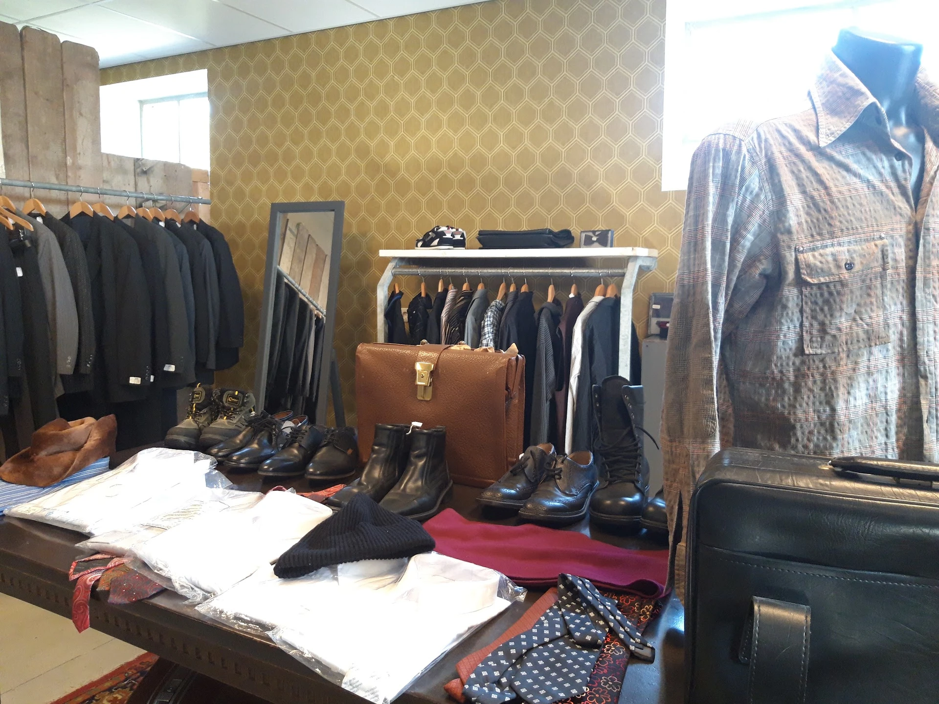 Uitgestalde tweedehands kleding, schoenen en accessoires in een kringloopwinkel, met jassen aan hangers en artikelen op tafel
