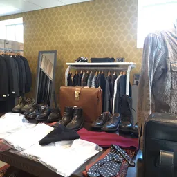 Uitgestalde tweedehands kleding, schoenen en accessoires in een kringloopwinkel, met jassen aan hangers en artikelen op tafel