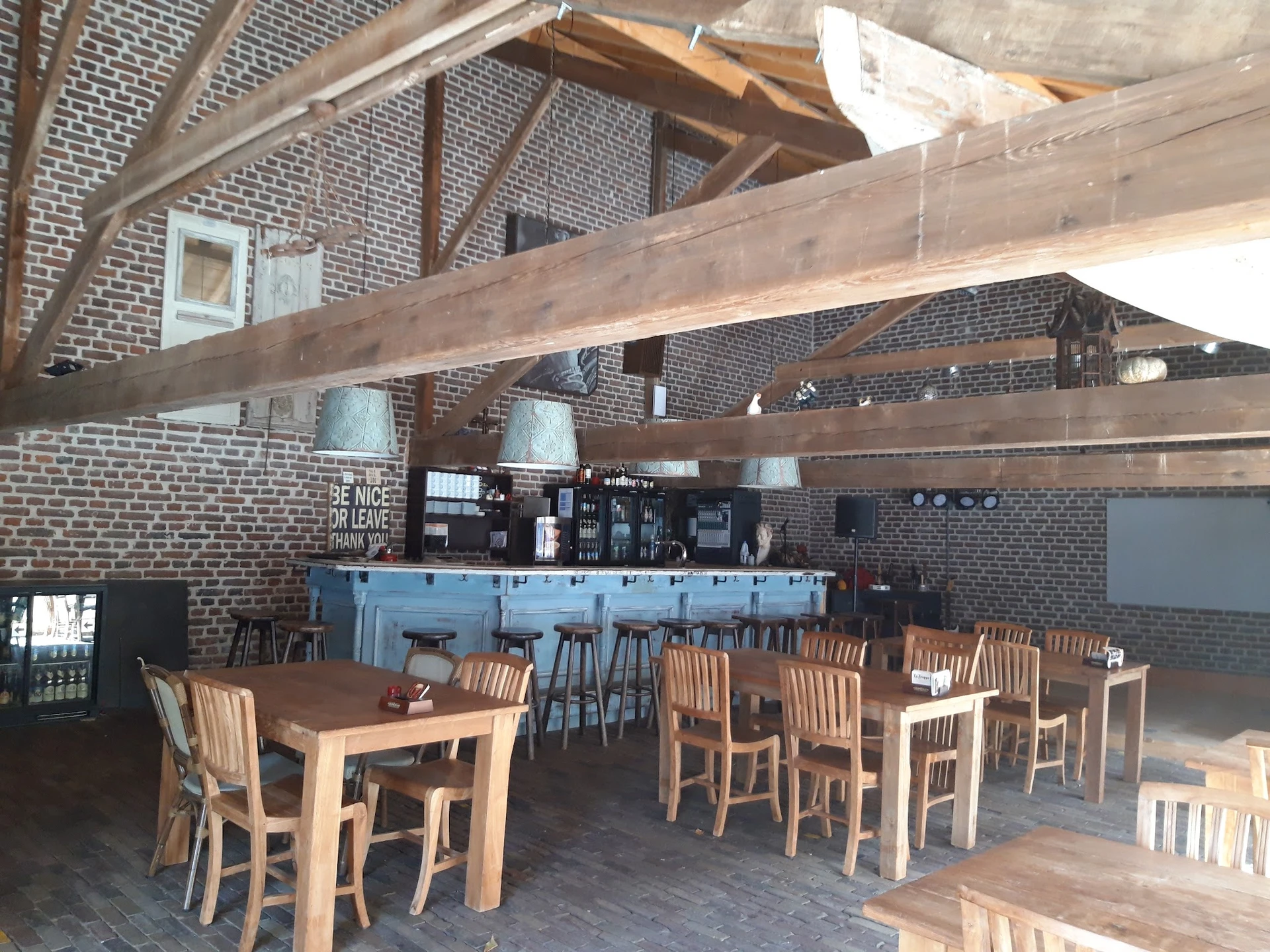 Lunchroom met houten tafels, stoelen en blauwe bar onder houten balkenplafond in bakstenen ruimte