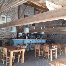 Lunchroom met houten tafels, stoelen en blauwe bar onder houten balkenplafond in bakstenen ruimte