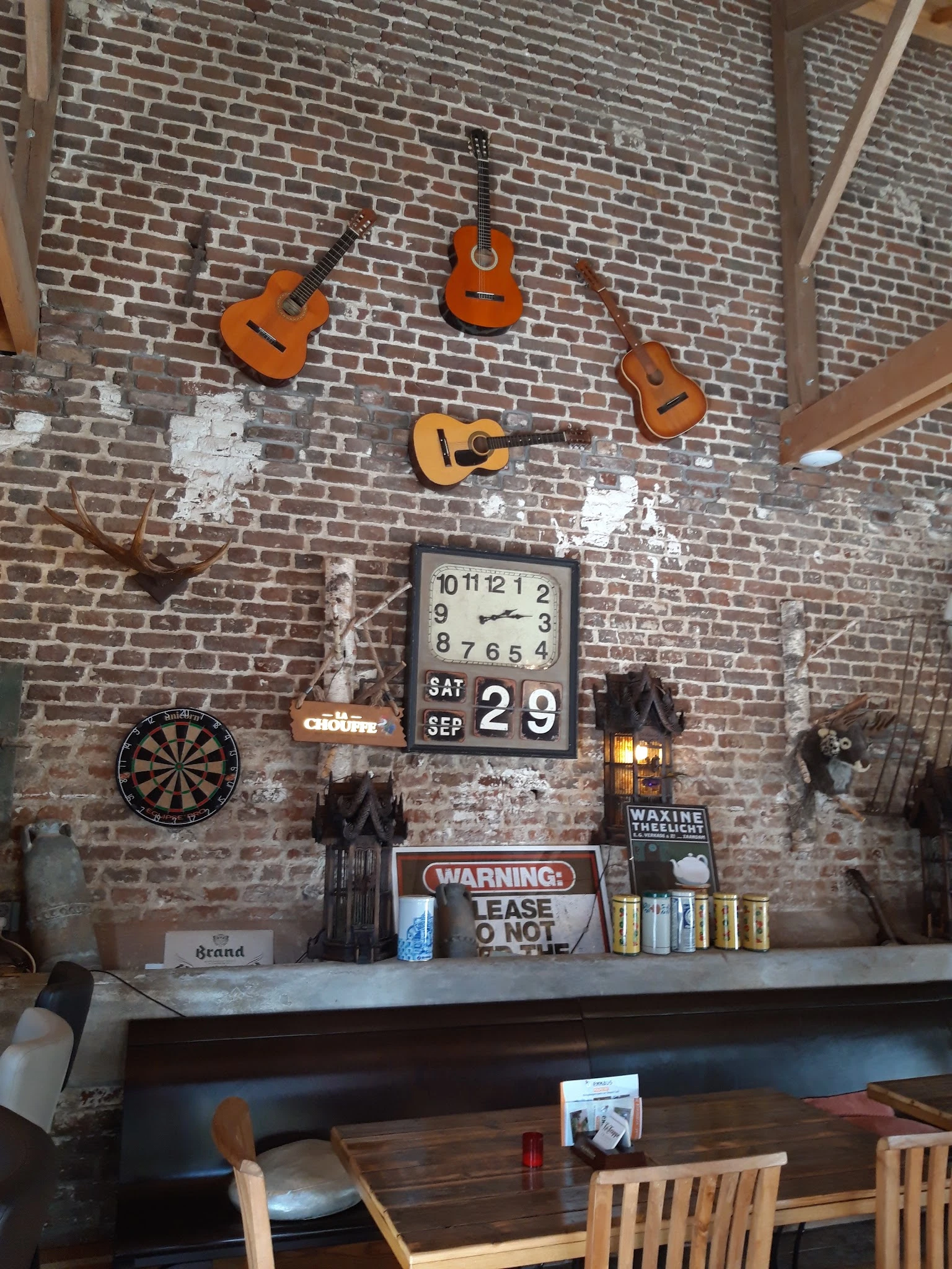 Bakstenen muur met decoratieve items zoals gitaren, klok, dartbord en waarschuwingsbord in kringloopwinkel