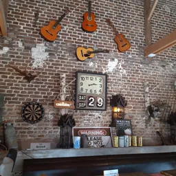 Bakstenen muur met decoratieve items zoals gitaren, klok, dartbord en waarschuwingsbord in kringloopwinkel