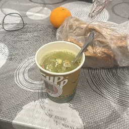 Kom soep met groenten in bekertje met lepel, brood in plastic zak op achtergrond