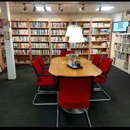 Binnenkant van kringloopwinkel met boekenkasten, tafel met rode stoelen en donkere vloer