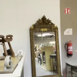 Interieur van kringloopwinkel met diverse tweedehands artikelen: decoratieve spiegels, vintage stoelen, een brandblusser en a