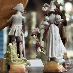 Twee vintage porseleinen beeldjes van meisjes in witte jurken met bruine details, van dichtbij gefotografeerd
