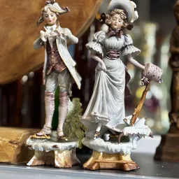 Twee decoratieve porseleinbeeldjes van een man en vrouw in historische kleding