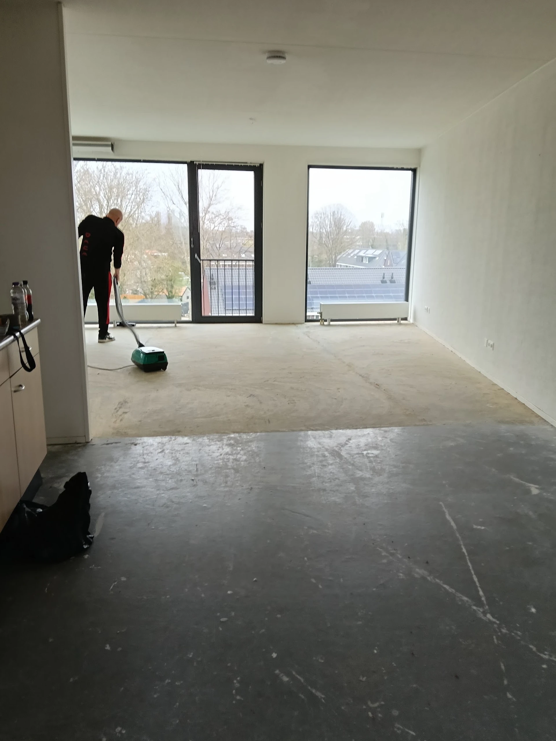 Lege winkelvloer onder renovatie met grote ramen en uitzicht op water, een persoon aan het werk met schoonmaakmateriaal