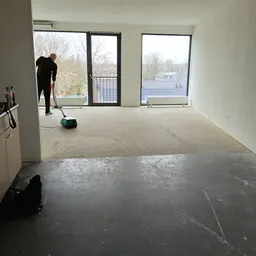 Lege winkelvloer onder renovatie met grote ramen en uitzicht op water, een persoon aan het werk met schoonmaakmateriaal