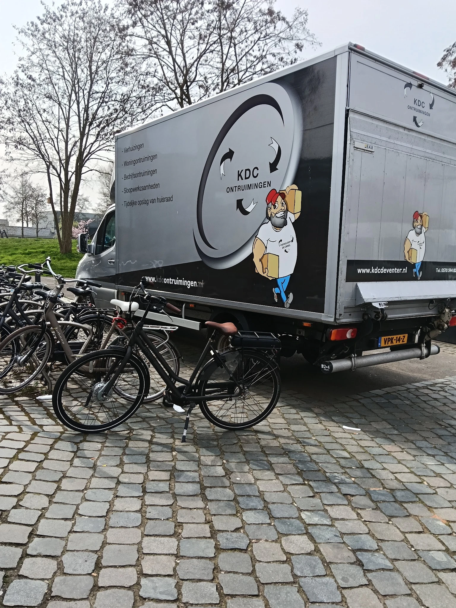 Bedrijfsbus van KDC Ontruimingen met cartoon-logo, geparkeerd naast fietsen op straat